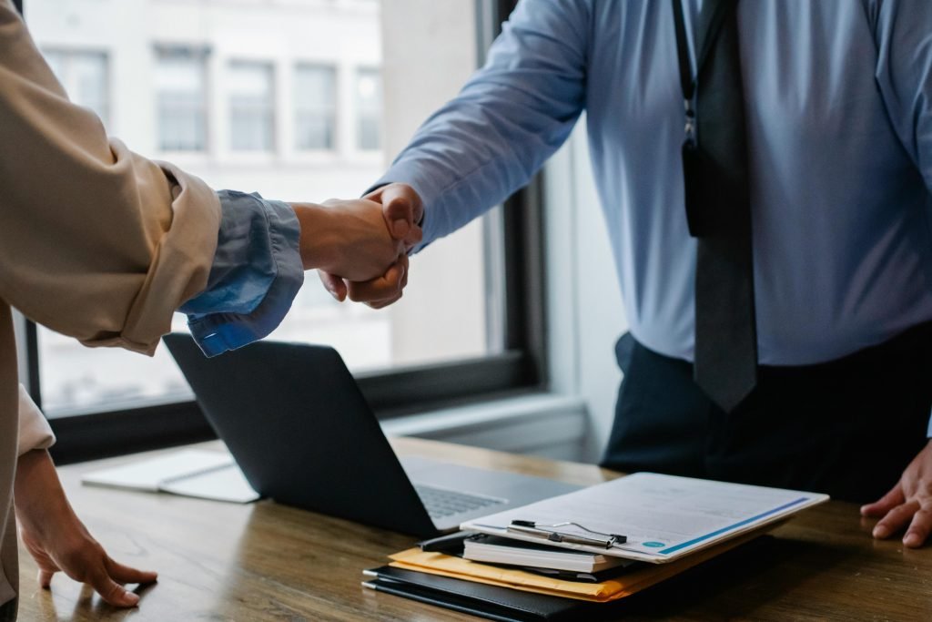 pexels-photo-5673488-5673488 Crop unrecognizable coworkers in formal wear standing at table with laptop and documents while greeting each other before meeting